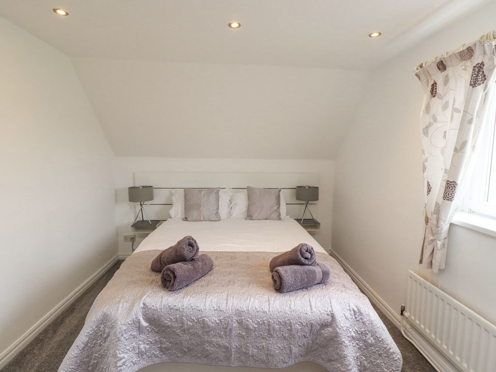 A bedroom with a double bed with pillows and rolled towels with table lamps on each side at Jara in Bamburgh
