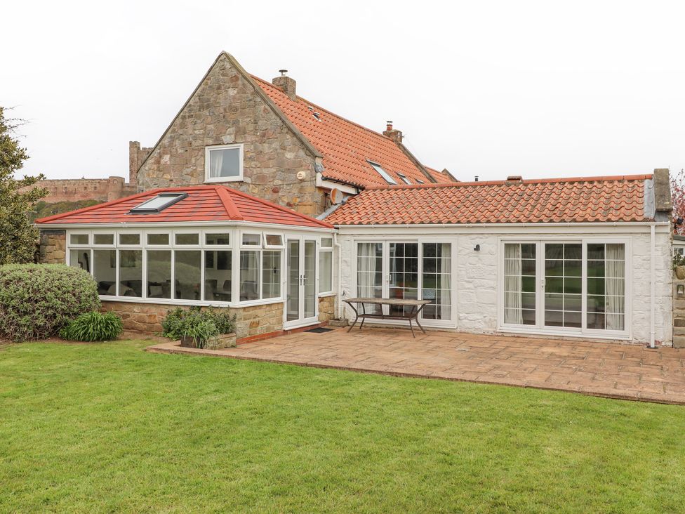 A stone house with multiple tiled roofs and large windows overlooking a patio and lawn at Jara in Bamburgh