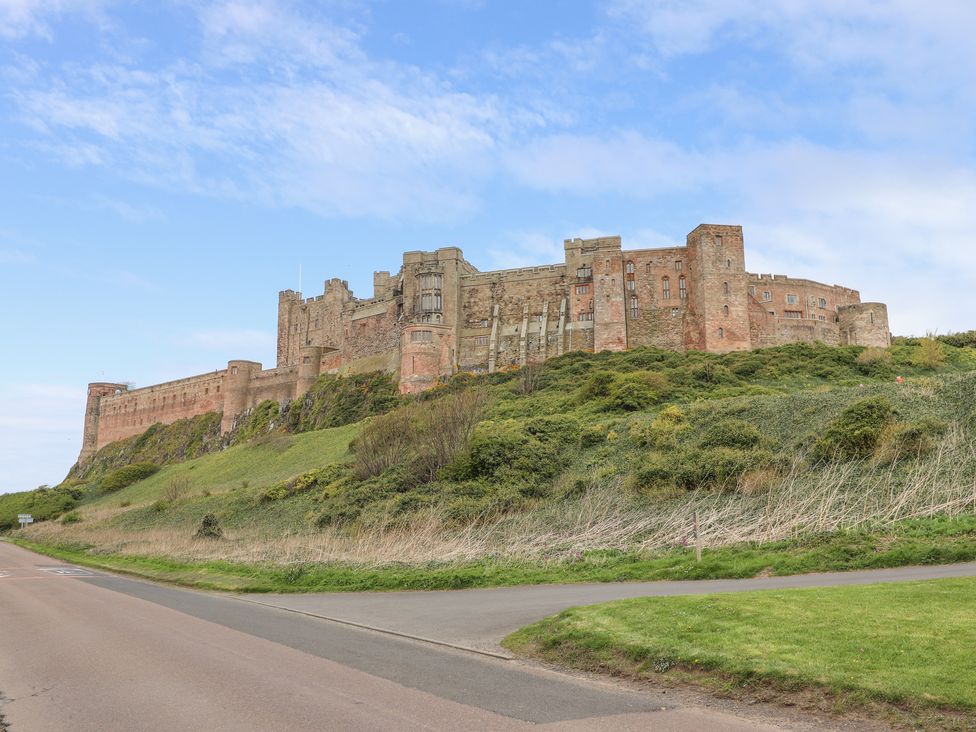 A large stone castle on a grassy hill next to a road at Jara in Bamburgh