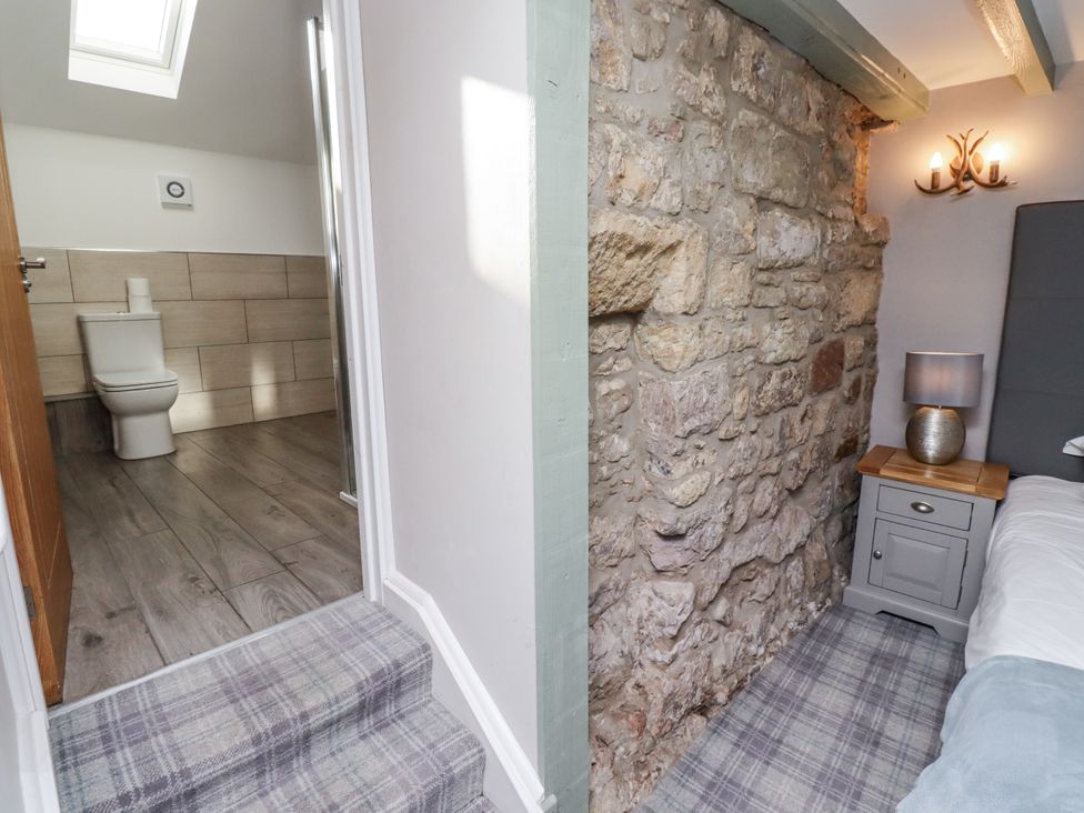 A bathroom with a toilet and shower next to a bedroom with a stone wall at Old Mill in Lucker
