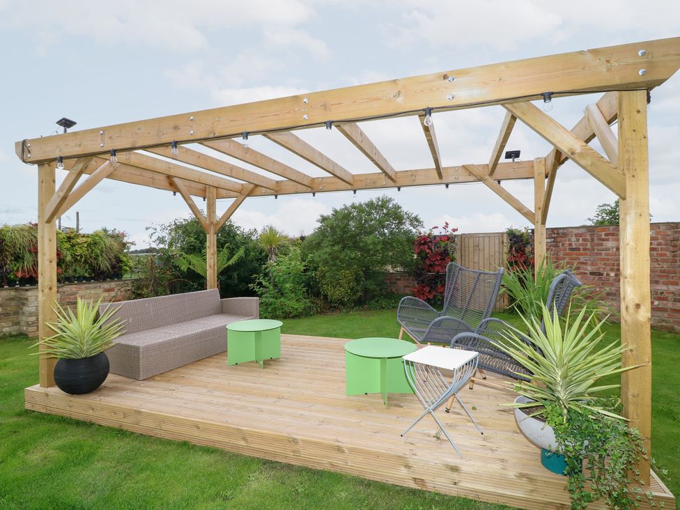 A garden with a wooden pergola and seating area at Hayloft in Scampton