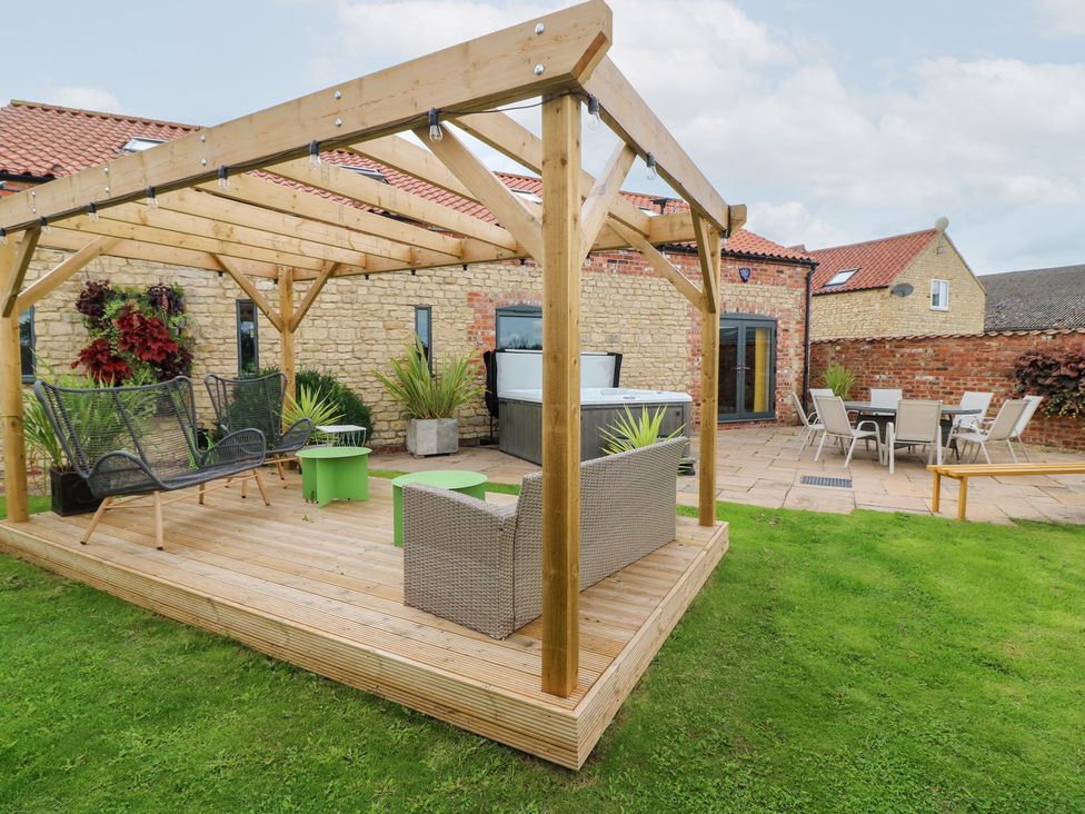 A garden with a wooden pergola and seating area at Hayloft in Scampton