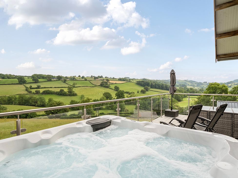 An outdoor area with a hot tub and chairs overlooking the countryside at Bwncath in Garthmyl