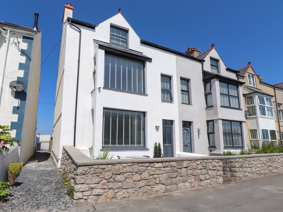 A house with multiple windows and a stone wall in front at Ty Haul in Rhosneigr