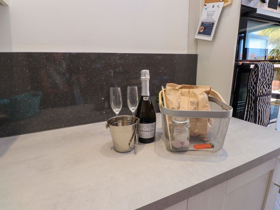 A kitchen countertop with champagne, glasses, and a basket at Ty Haul Rhosneigr