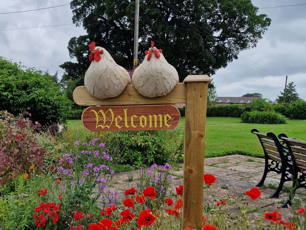 A welcome sign with chickens and flowers in a garden at How Hill Farm Cottage Greystoke