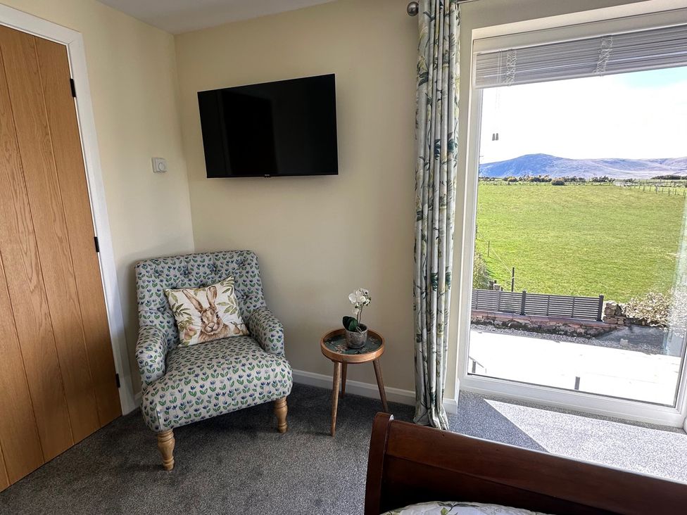 A bedroom with a TV and an armchair at How Hill Farm Cottage in Greystoke