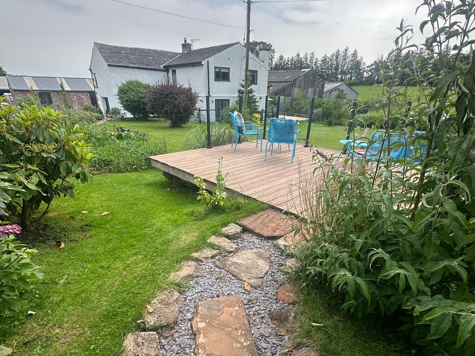 A garden with a house and deck in the background at How Hill Farm Cottage in Greystoke
