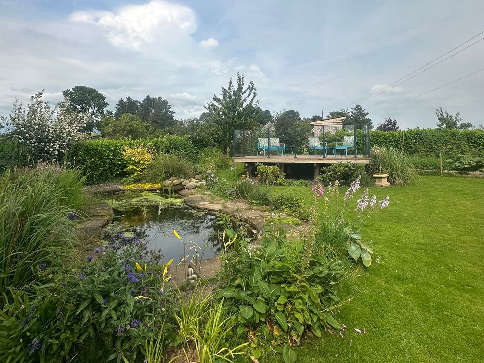 A garden with a pond and a deck with chairs at How Hill Farm Cottage Greystoke
