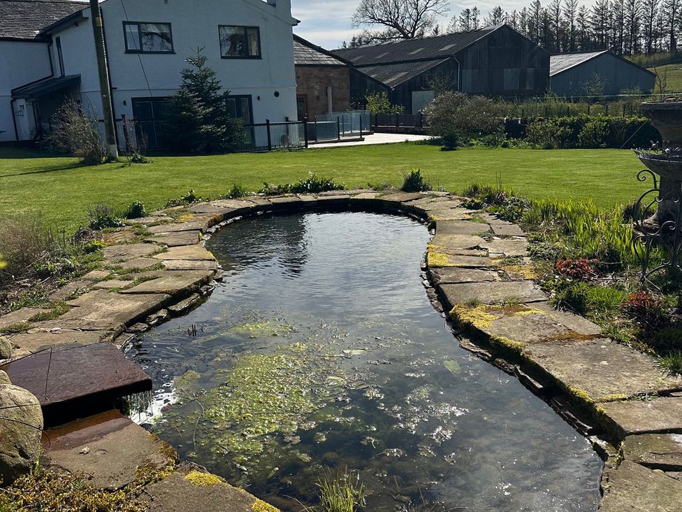 A pond with a stone pathway and grass at How Hill Farm Cottage in Greystoke