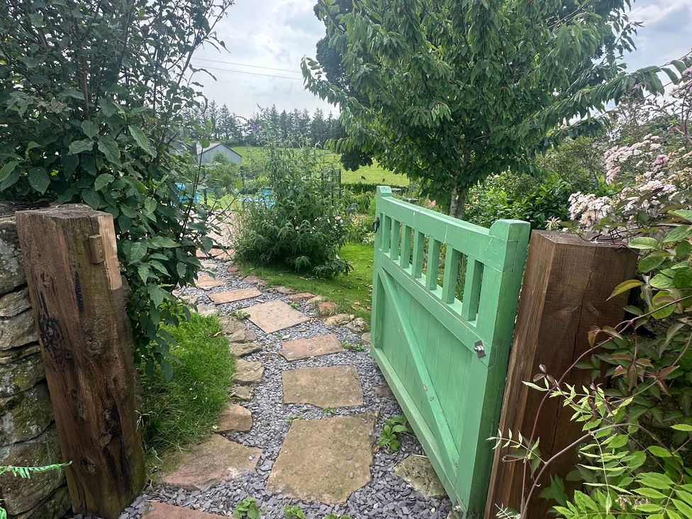 A garden with a green gate and stone pathway at How Hill Farm Cottage Greystoke
