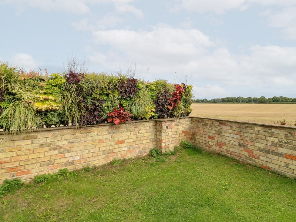 A garden with a brick wall and hedge at Hideaway in Scampton