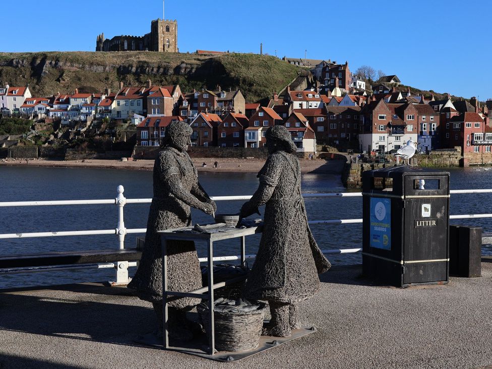 Two statues interacting at the waterfront with buildings and a castle in the background at 5 Hall Yard Whitby