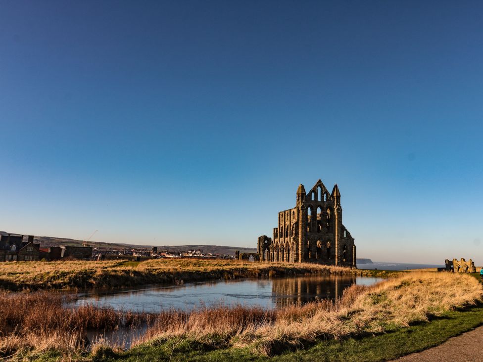 Ruins near water with grass and buildings at 5 Hall Yard in Whitby