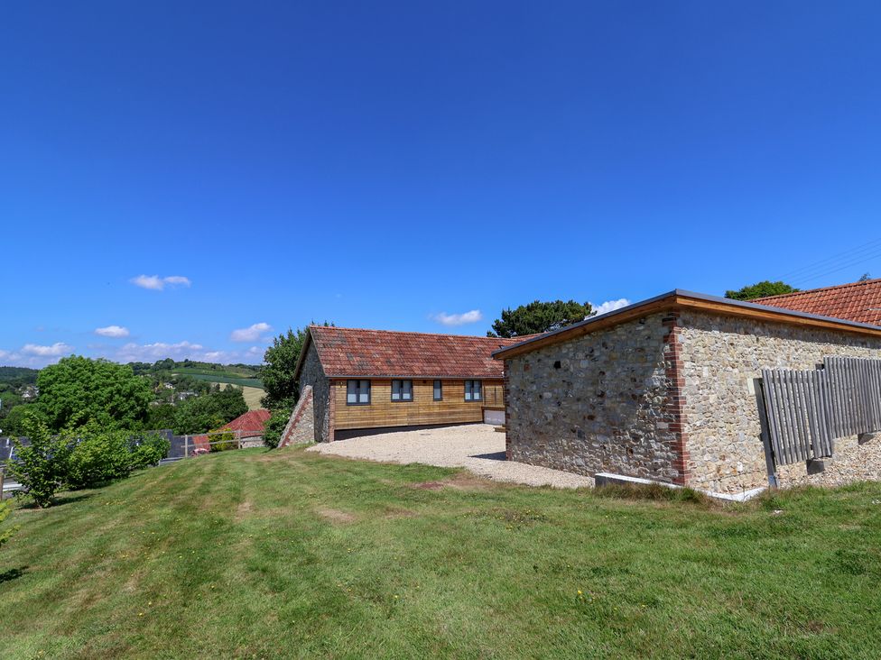 A view of two buildings and grass under a clear sky at The Stables in Uplyme