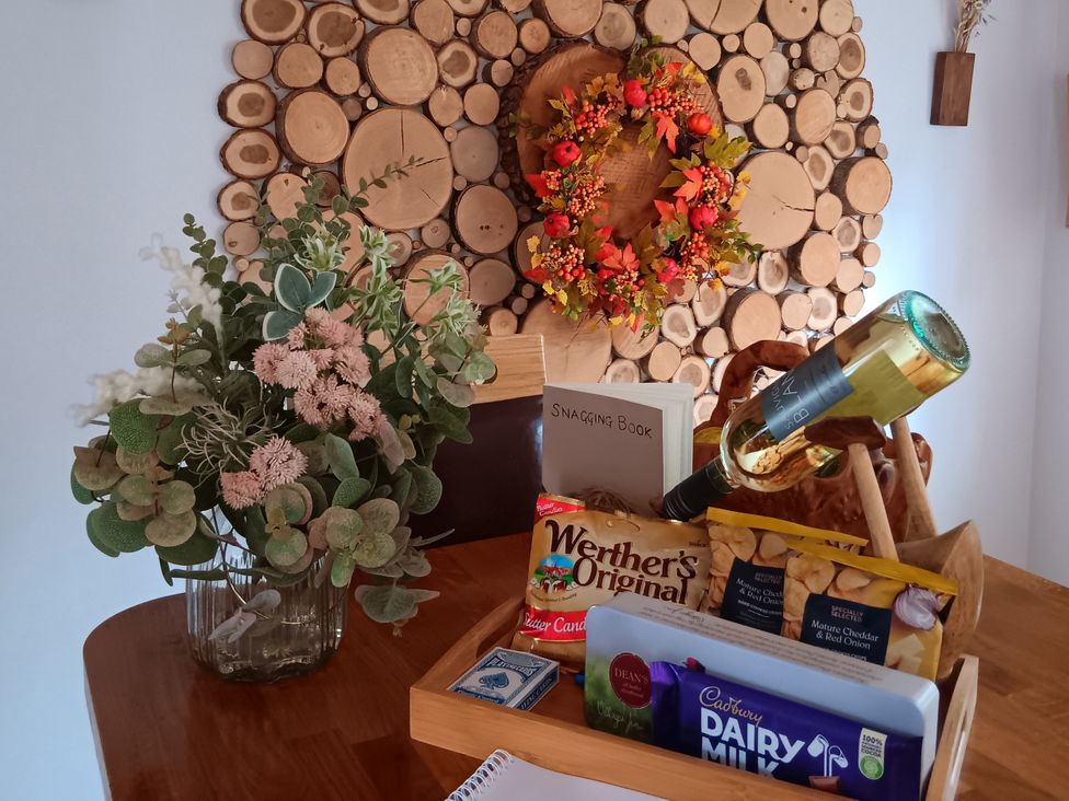 A dining room table with flowers, wine bottle, and snack items at Tawny Owl Cottage North Somercotes