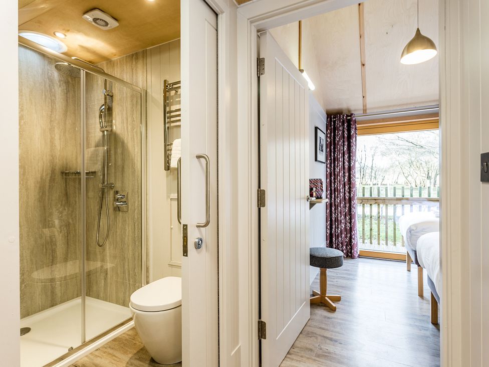 A bathroom with a shower and toilet next to a bedroom with a bed and window at Lodge 15 Corfe Castle