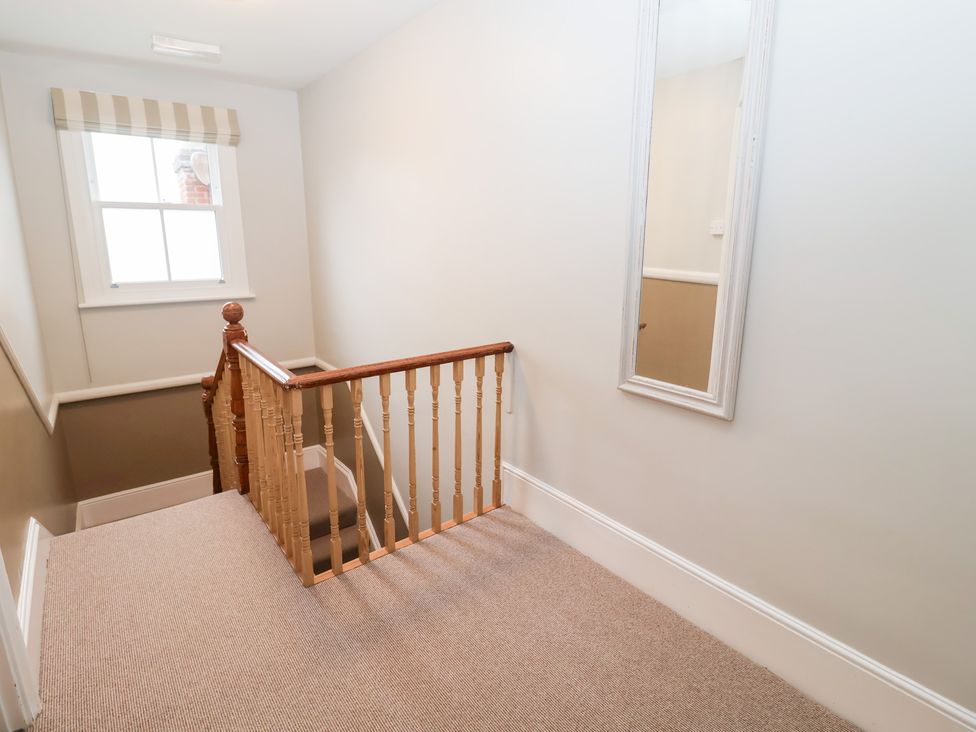 A hallway with a staircase and a mirror at Elkhorn in Southwold