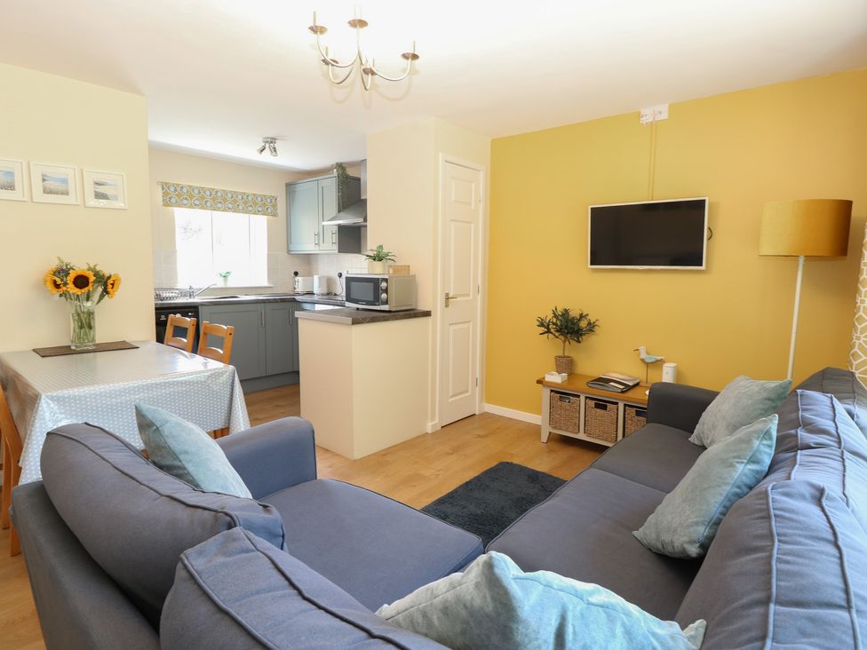 A living room with a sofa and dining area at 15 The Dell Mundesley