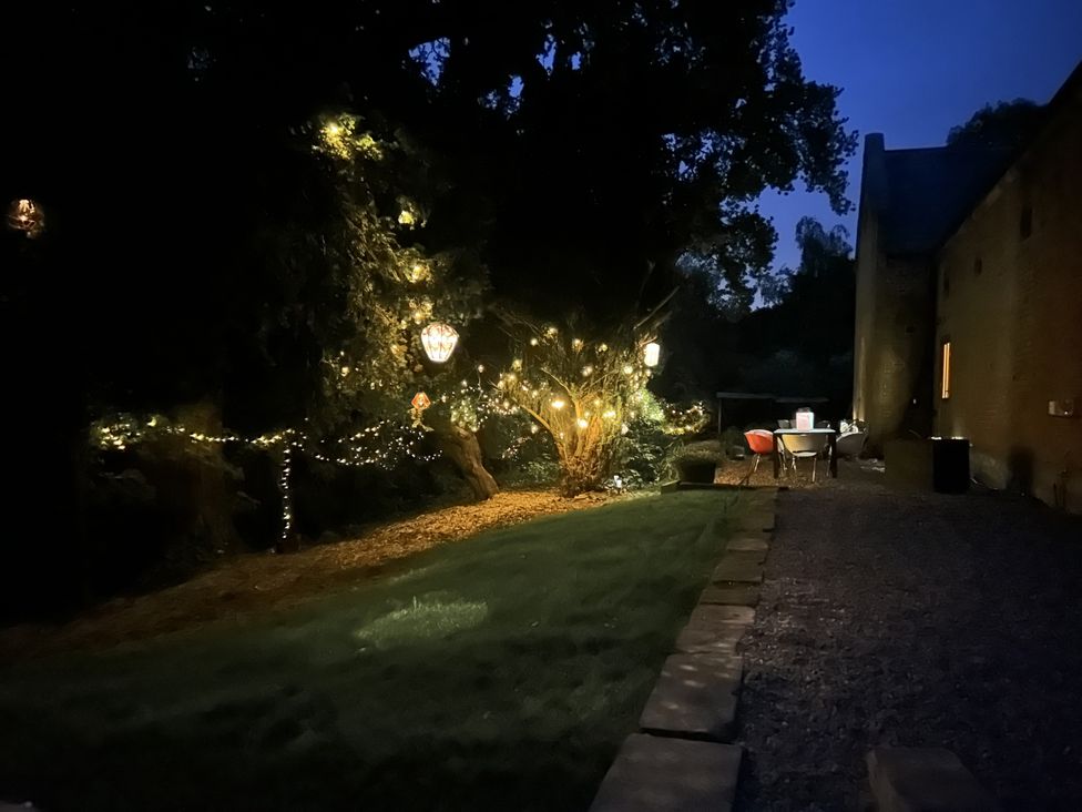 An outdoor garden area at night with string lights on trees and a table with chairs near a building at Chetwynd Lodge Ingestre near Great Haywood