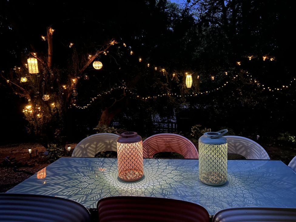An outdoor table with lanterns casting patterned light and string lights hanging in the trees at Talbot Lodge in Ingestre near Great Haywood