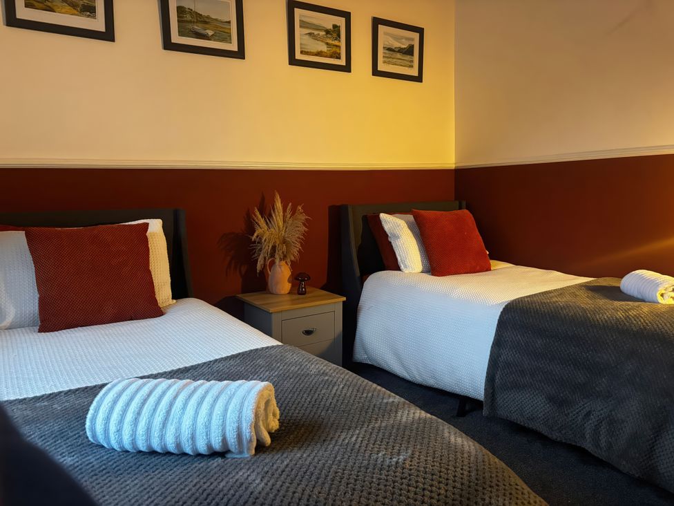 A bedroom with two single beds and framed pictures at Heol Madog in Porthmadog