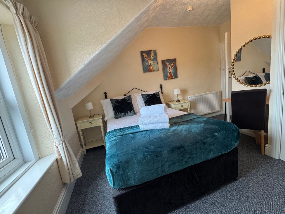A bedroom with a bed, nightstand, lamp, and desk at The Causeway