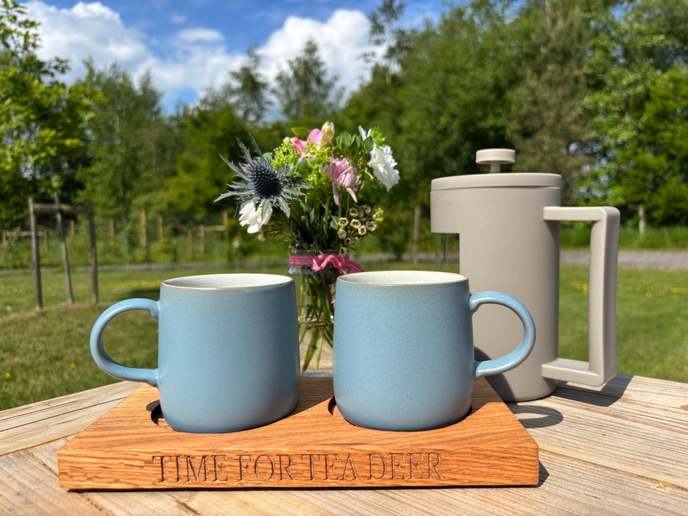 Two blue mugs and a beige French press on a wooden tray with flowers in a jar outside on a wooden table at Oh Deer in Ashbourne
