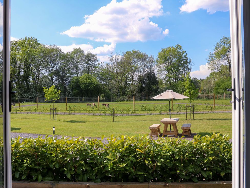 A garden with picnic table umbrella small benches and trees viewed through open glass doors at Oh Deer in Ashbourne