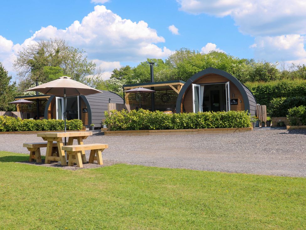 Two wooden camping pods with open doors and umbrellas in front near picnic tables at Oh Deer in Ashbourne