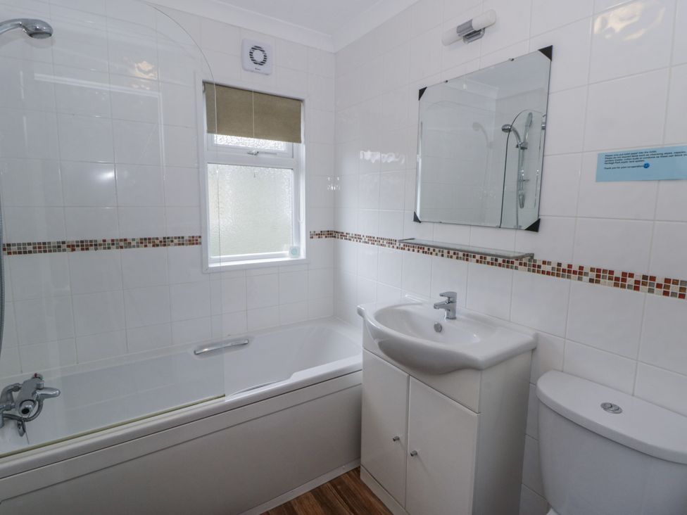 A bathroom with a bathtub, sink, toilet, and mirror at Seacroft in Stepaside near Kilgetty
