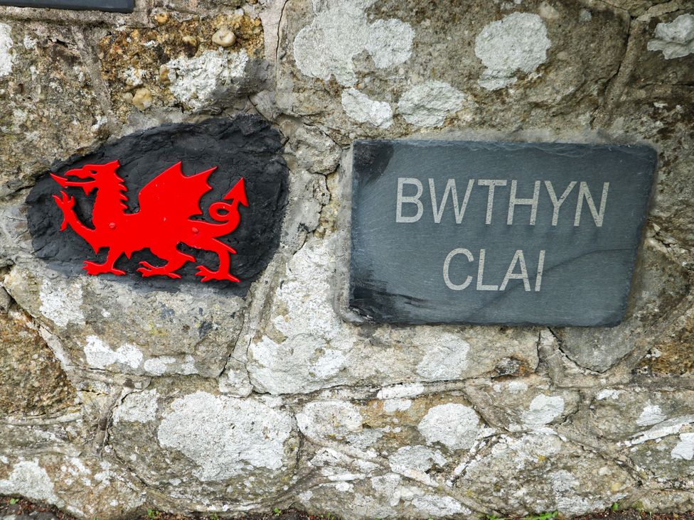 A dragon sign and a slate sign with Bwthyn Clai on a stone wall