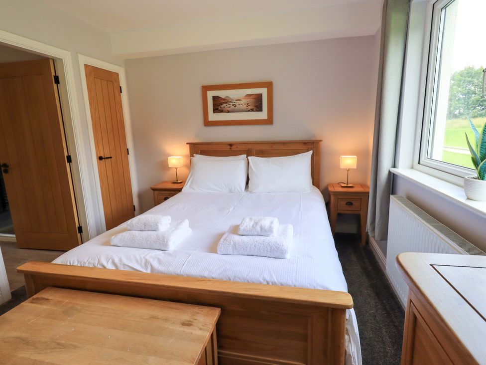 A bedroom with a bed, nightstands, and a window at Mallard Cottage, Penrith
