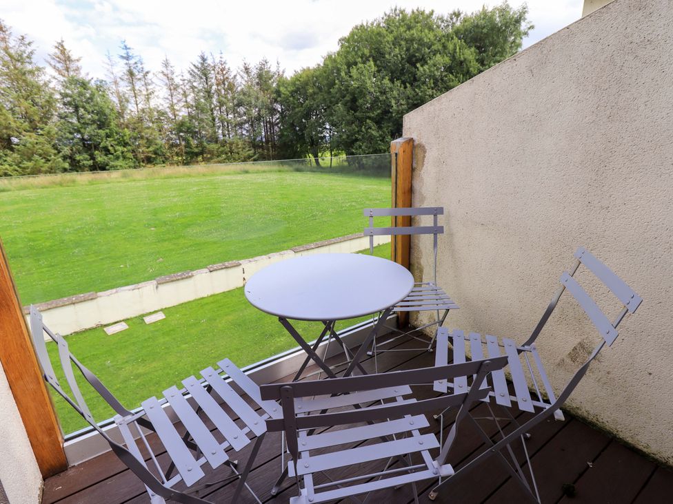 A balcony with a table and chairs overlooking a grassy area at Mallard Cottage Penrith