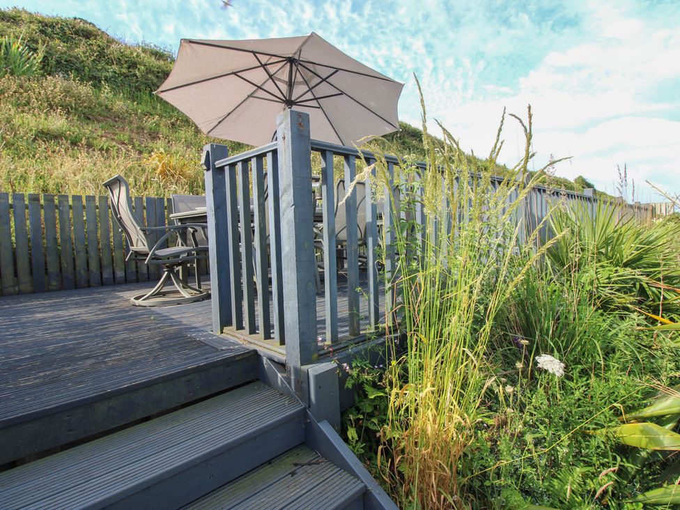 An outdoor deck with a table and chairs under an umbrella at 7 Beachdown in Challaborough