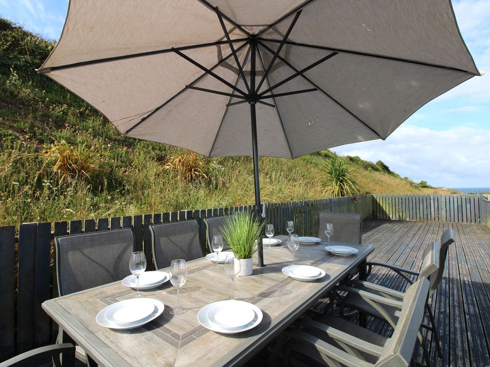 An outdoor dining table with chairs and an umbrella at 7 Beachdown in Challaborough