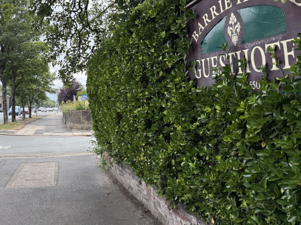 A view of a street with a hedge and a guesthouse sign at The Furness Haven in Barrow-In-Furness
