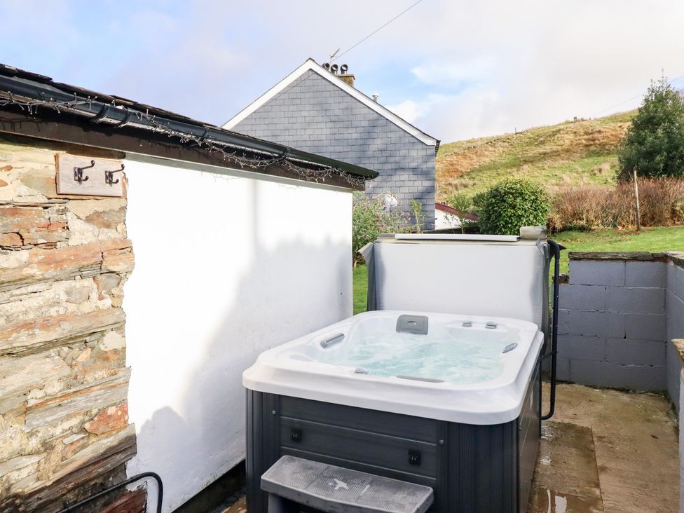 An outdoor area with a hot tub near a stone wall and grass at Ael Y Bryn Ffestiniog