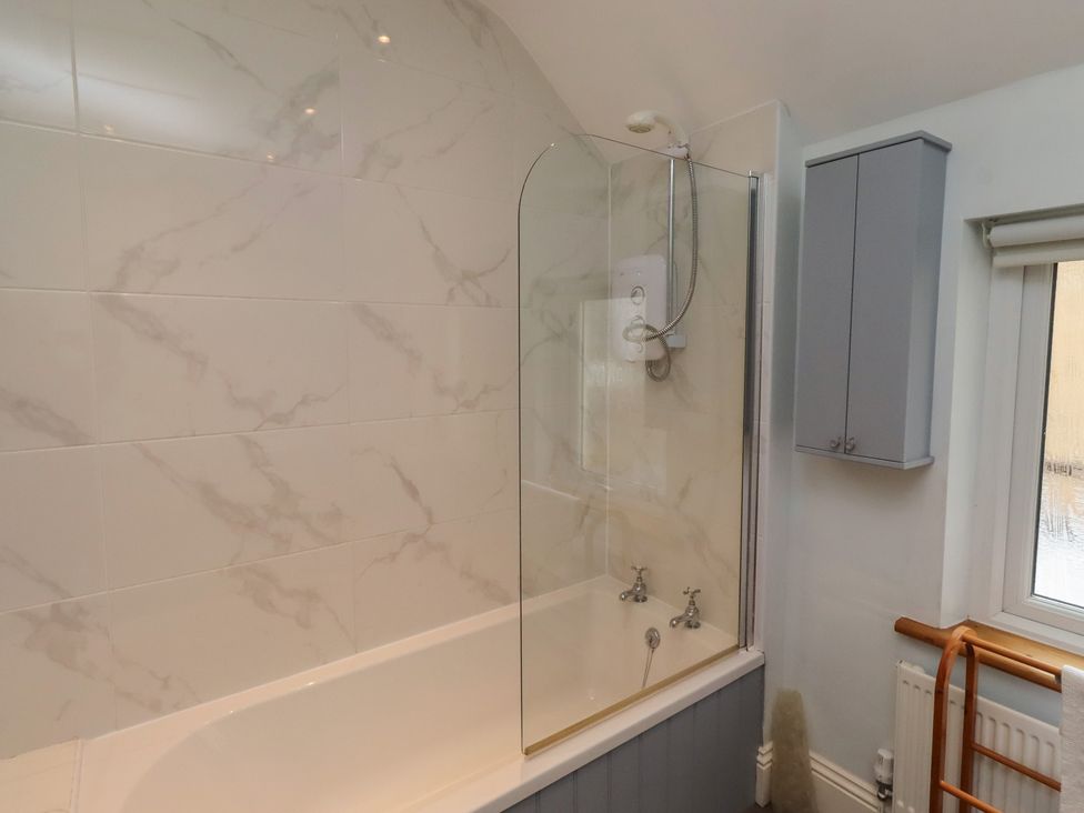 A bathroom featuring a bathtub with a shower and a wall cabinet at Rose House Alnmouth