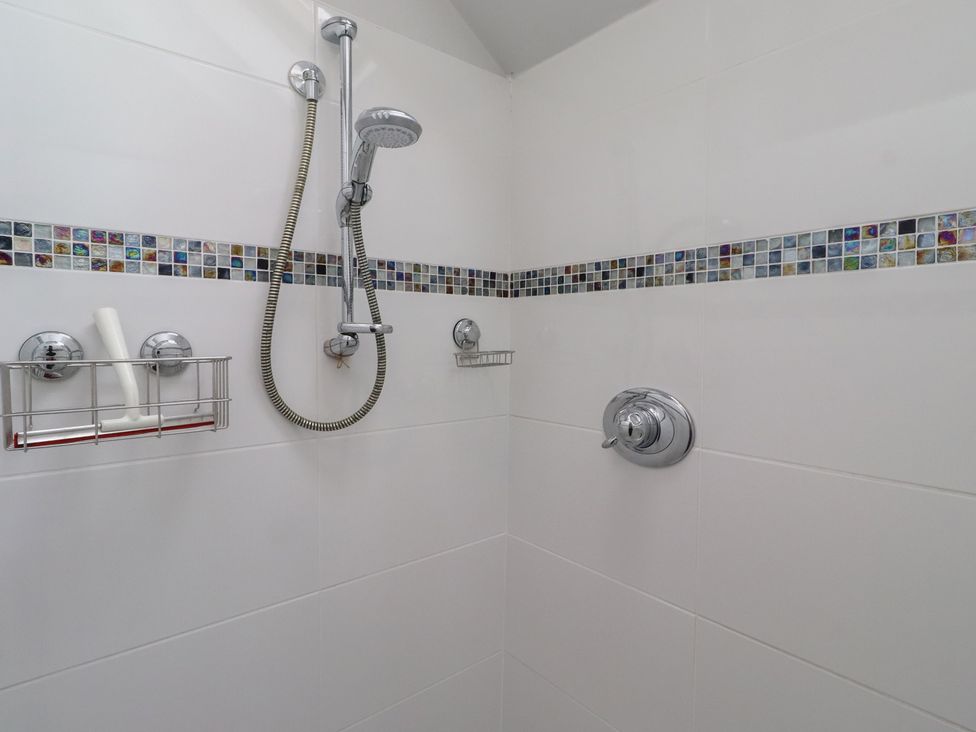 A shower with decorative tiles and shower fixtures at Rose House Alnmouth