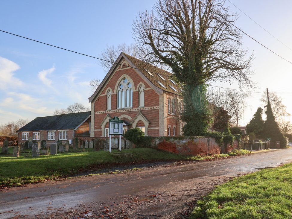 A building with a signboard and trees near a gravel road at The Stables at Hall Barn near Wattisfield near Walsham-Le-Willows