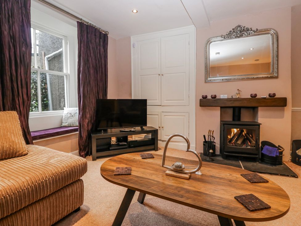 A living room with a sofa, coffee table, television and fireplace at The Old Book Shop in Cartmel