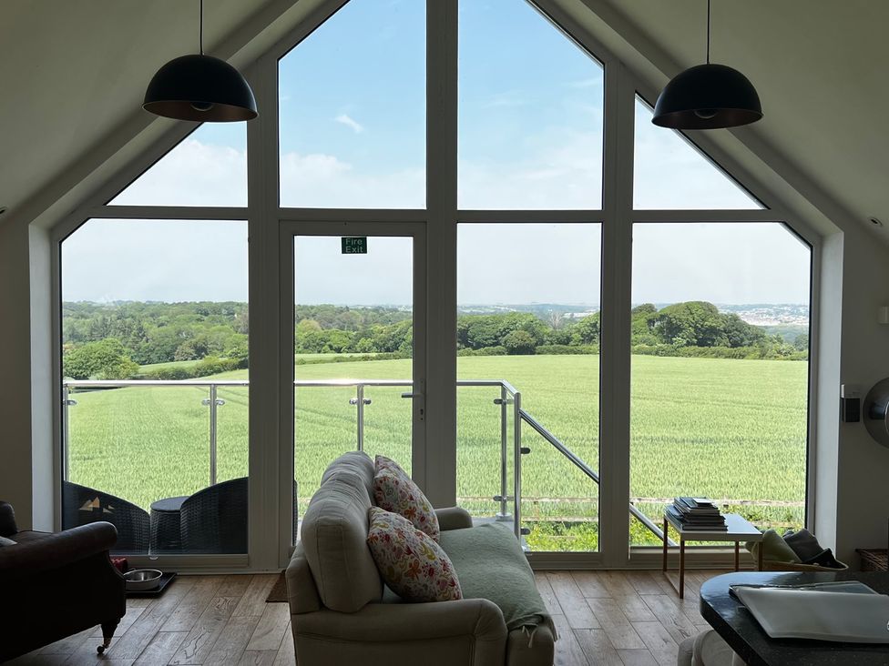 A living room with large windows overlooking a field at Spires in Playing Place near Carnon Downs