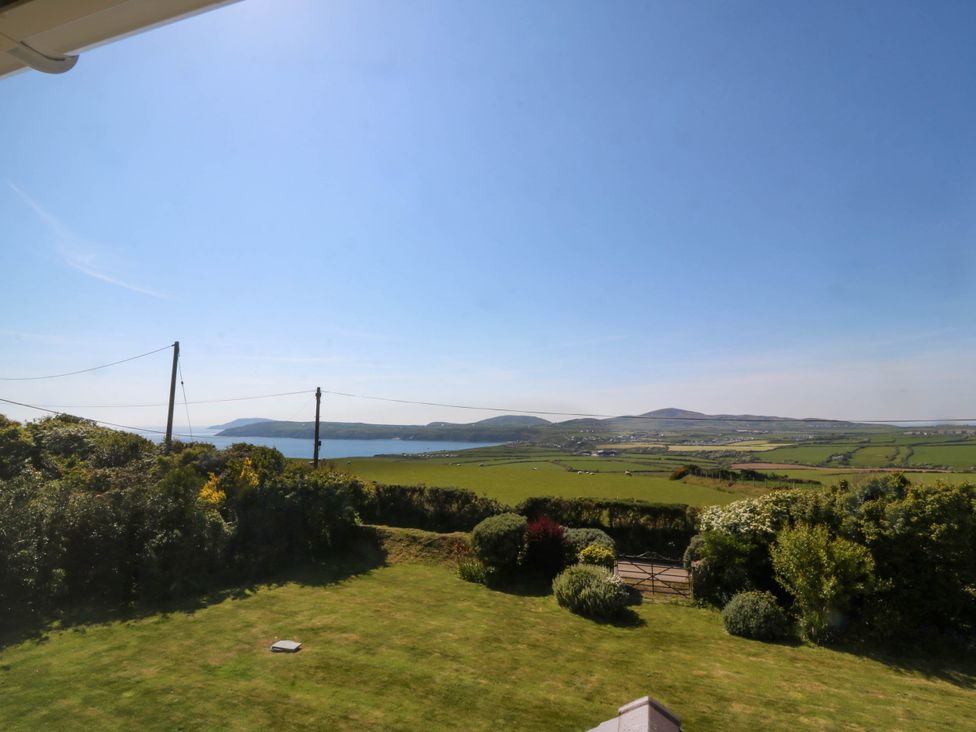 A view of a garden with bushes and a gate overlooking fields hills and water at Ael Y Fron in Aberdaron