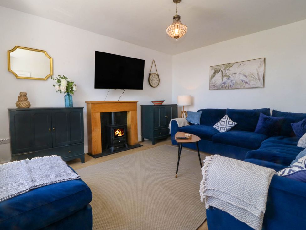 A living room with a fireplace a wall-mounted tv blue sofas round wooden side table and two cabinets at Ael Y Fron in Aberdaron