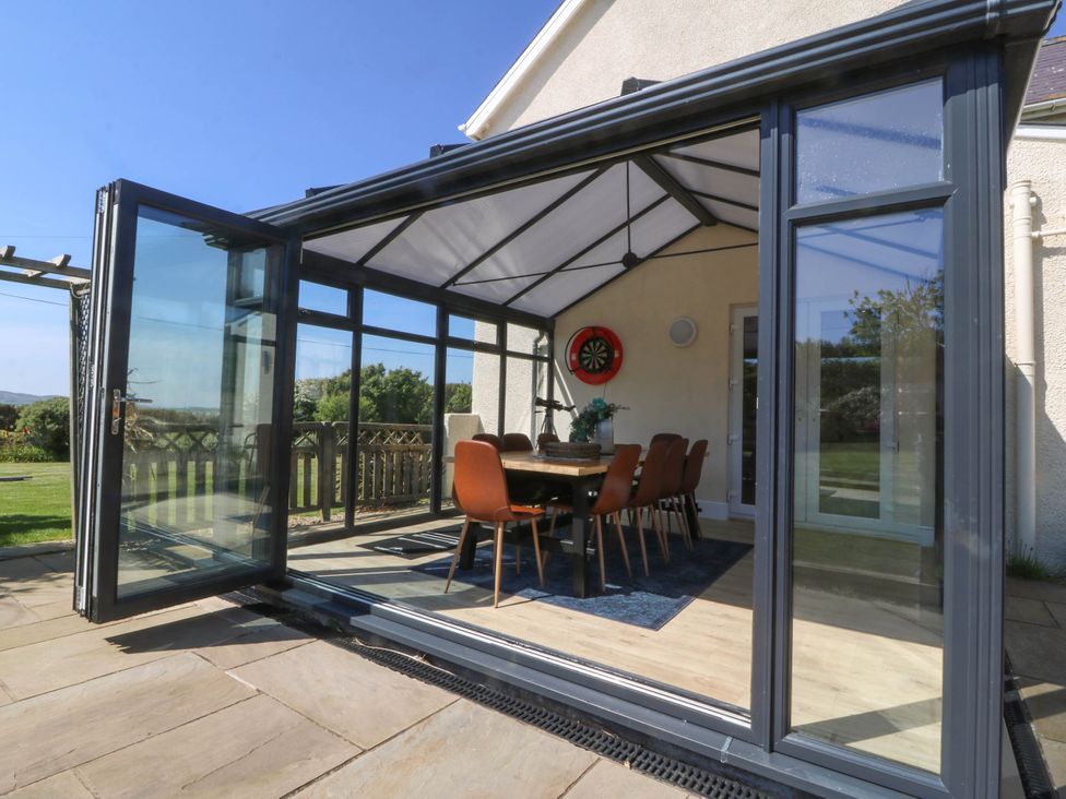A glass conservatory with an open door containing a dining table and chairs at Ael Y Fron in Aberdaron