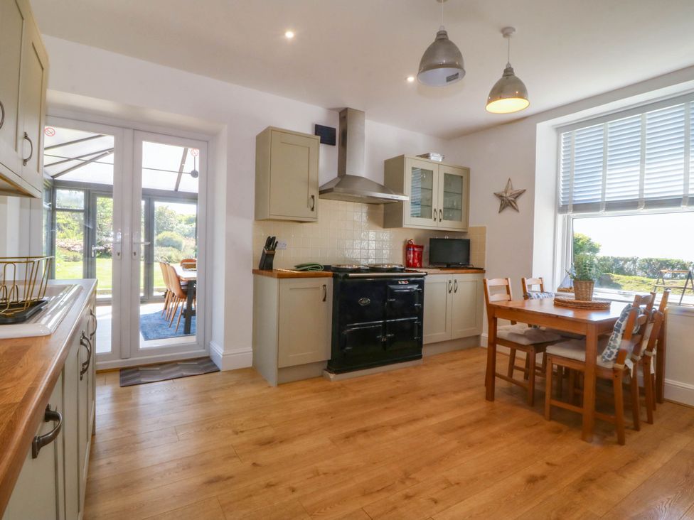 A kitchen with wooden floors a dining table with chairs a black oven and glass doors leading outside at Ael Y Fron in Aberdaron