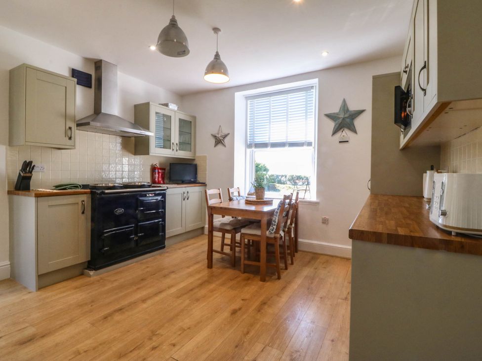 A kitchen with wooden floor cabinets stove dining table and chairs near a window at Ael Y Fron in Aberdaron