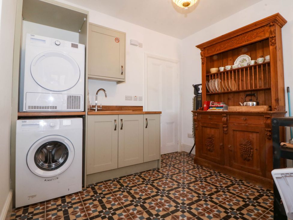 A utility room with washing machine and dryer next to wooden cabinet with dishes at Ael Y Fron in Aberdaron