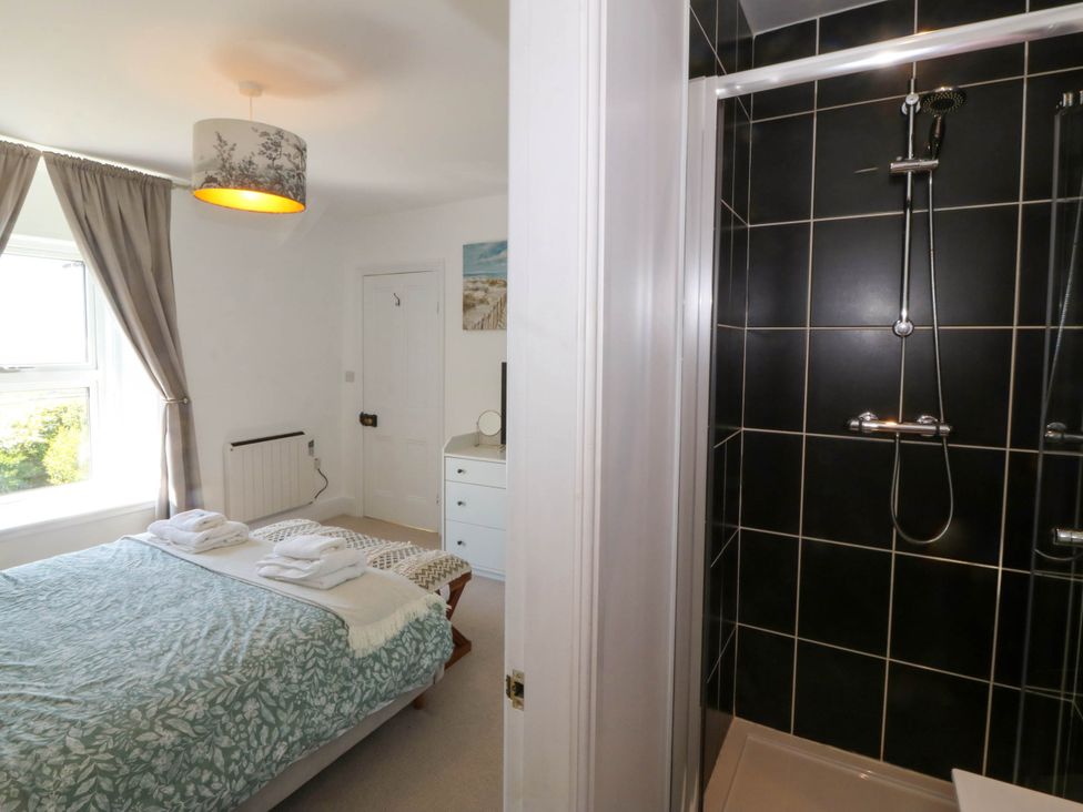 A bedroom with a bed and folded towels next to a shower with black tiles at Ael Y Fron in Aberdaron